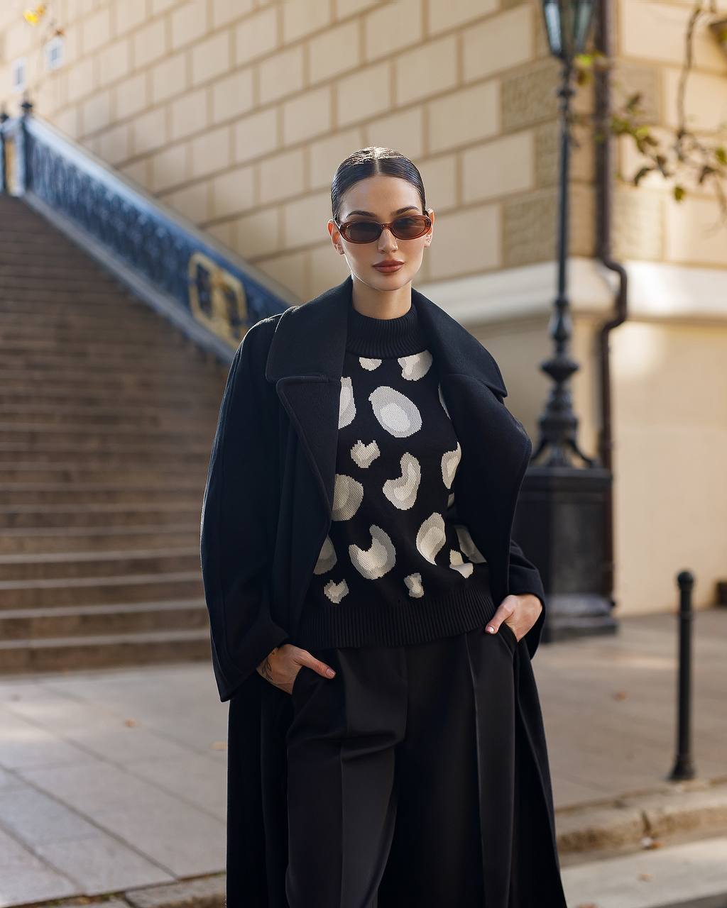 Woman wearing a black coat and patterned black sweater in an urban setting