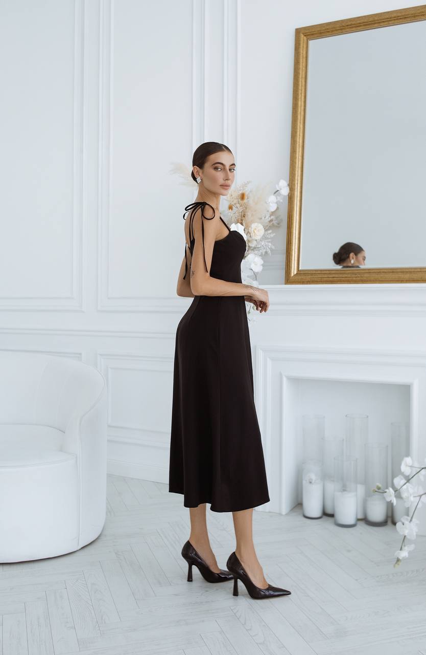 Woman in a black dress standing in a white room with a mirror.