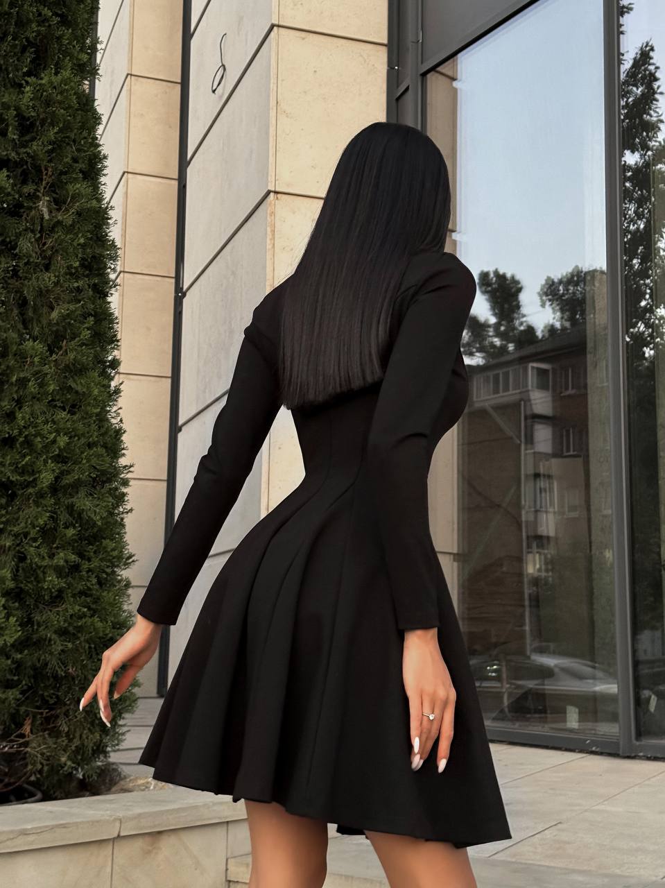 Person wearing a black dress standing outside a building with large windows.