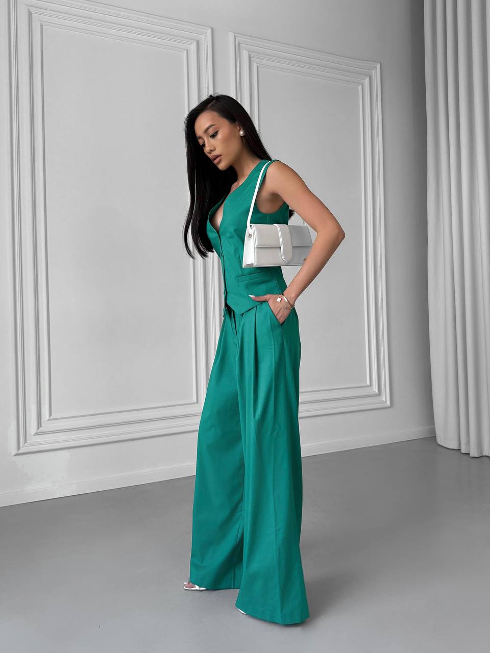 Woman in a teal jumpsuit standing against a gray wall.