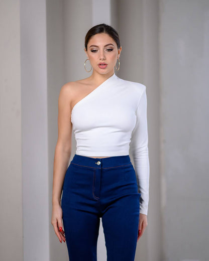 Woman wearing a white one-shoulder top and blue pants against a plain background