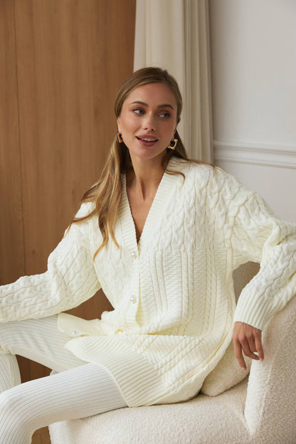 Woman wearing a white cable knit sweater and pants sitting on a chair.