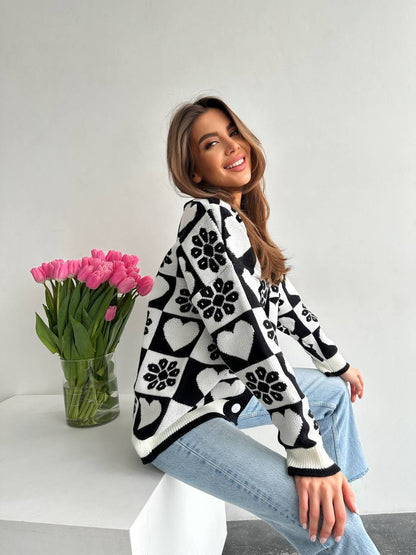 Woman wearing a black and white patterned sweater sitting on a white chair with pink tulips in the background.