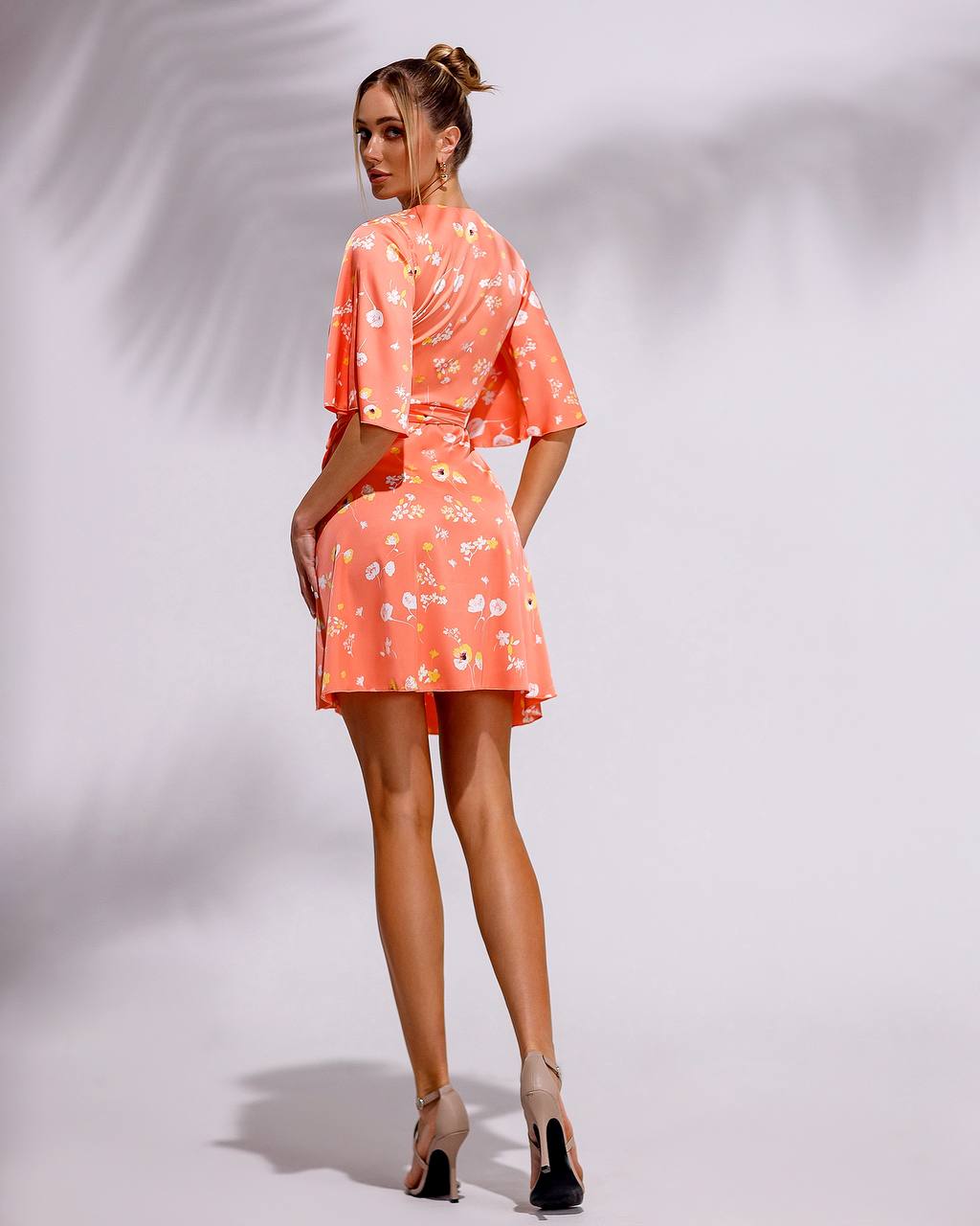 Woman wearing a coral floral dress on a white background