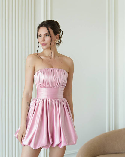 Woman wearing a pink strapless dress against a white wall