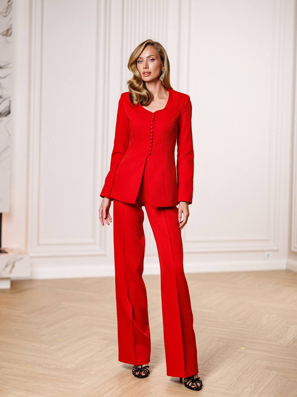 Woman wearing a red suit standing in a room with white paneled walls.
