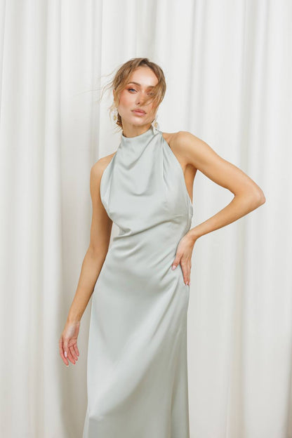 Woman wearing a light blue halter neck dress against a white curtain background