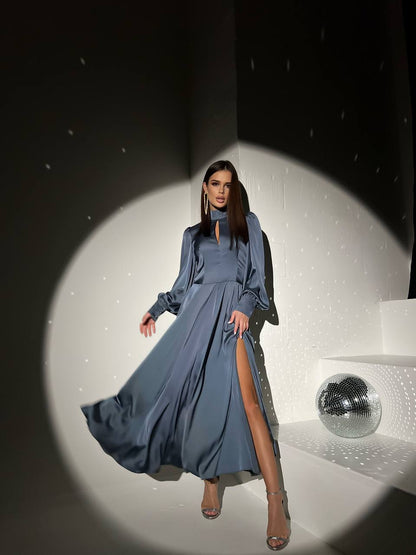 Woman in a long blue dress with a high slit standing in front of a mirror on a reflective surface.