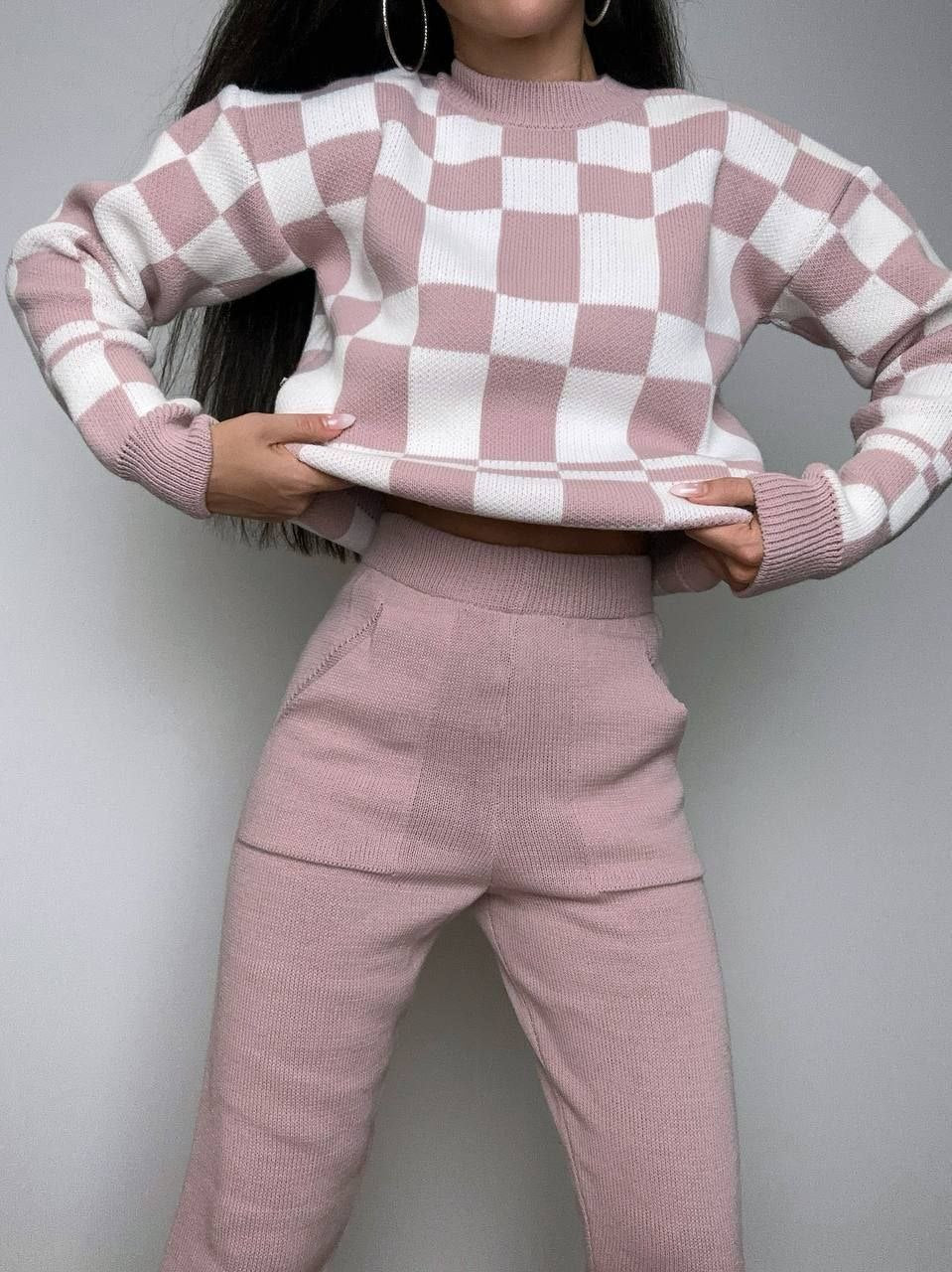Person wearing a pink and white checkered sweater and pants against a gray background