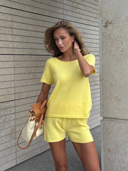 Woman wearing a yellow outfit standing against a light-colored wall.