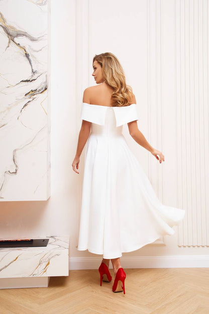 Woman in a white off-shoulder dress with red high heels standing in a room with marble wall.