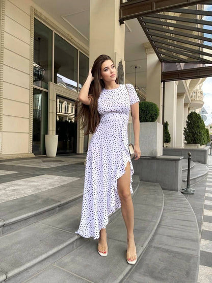 Woman in a white dress with black polka dots standing on steps outside a building.