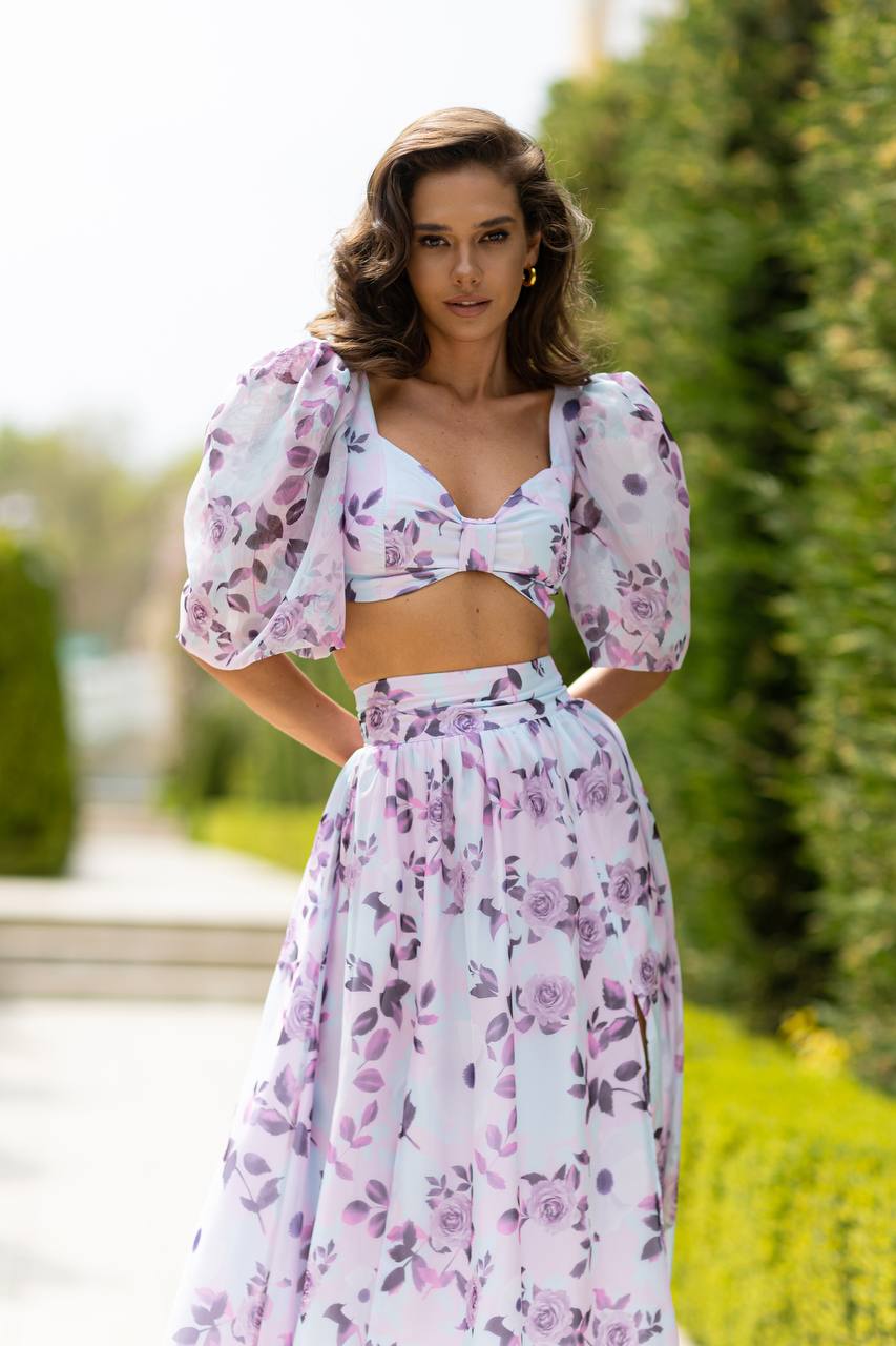 Woman wearing a floral two-piece outfit standing outdoors with greenery in the background