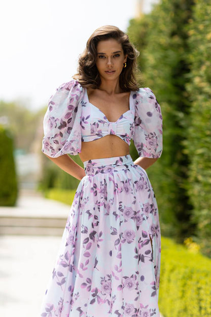 Woman wearing a floral two-piece outfit standing outdoors with greenery in the background