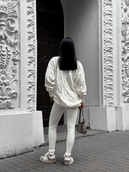Person wearing a white jacket and pants walking past ornate stone walls.