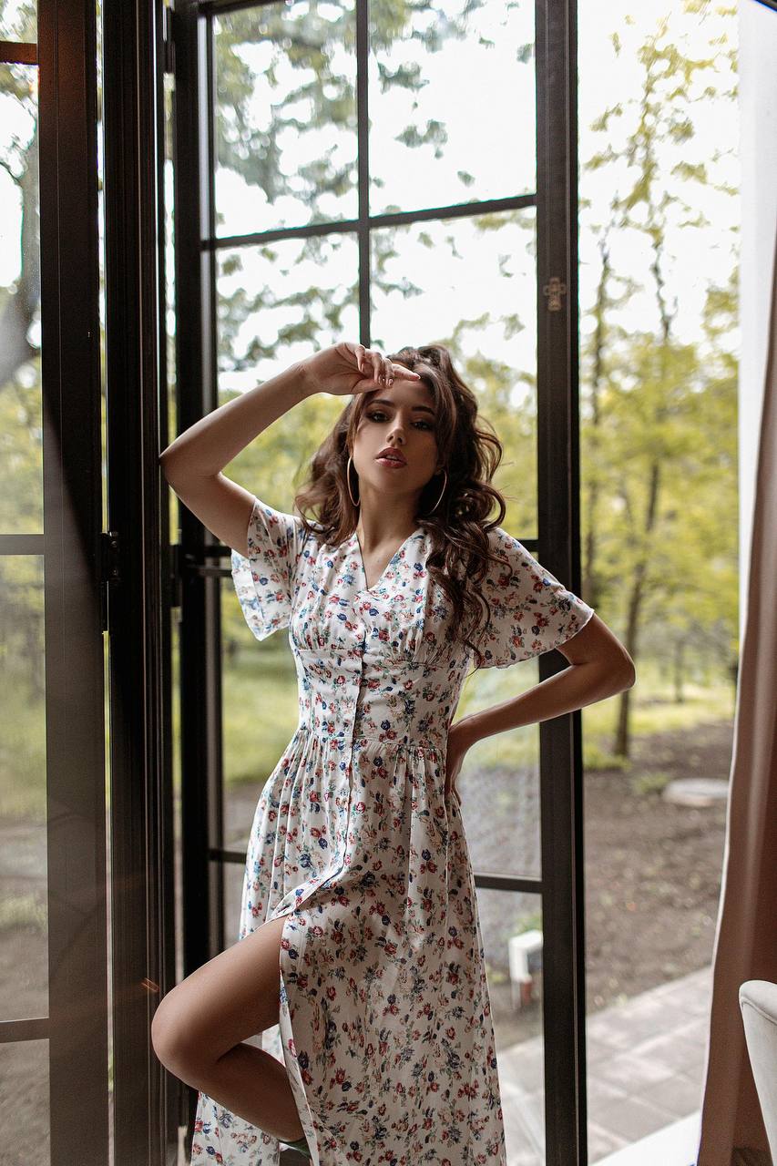 Woman in a floral dress standing by a glass door with a natural outdoor background