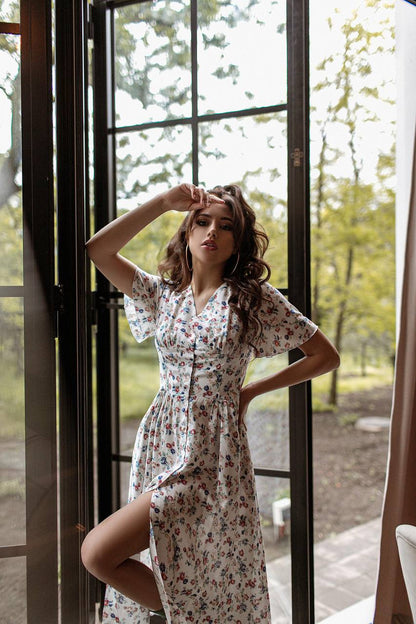 Woman in a floral dress standing by a glass door with a natural outdoor background