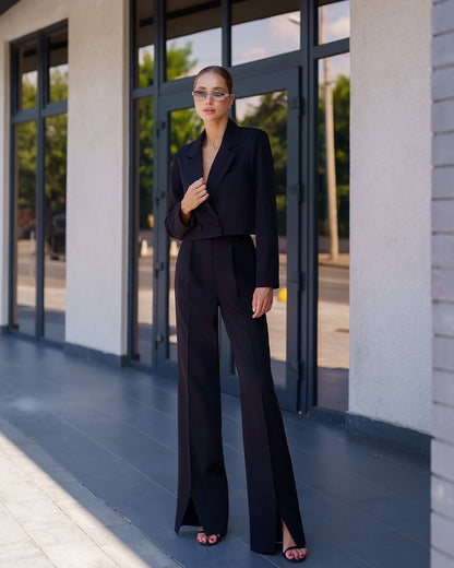 Woman in a black suit standing outside a building with large windows.