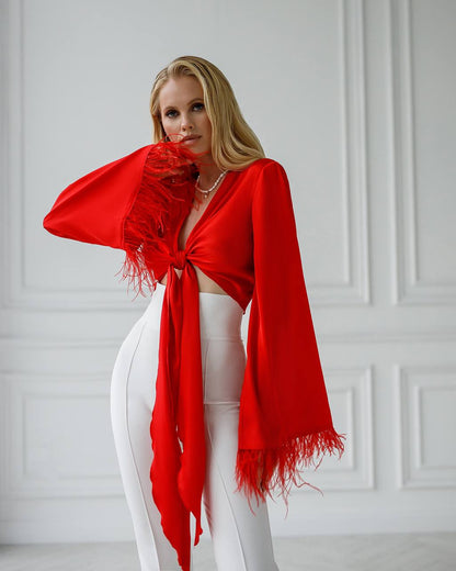 Woman wearing a red scarf and white pants against a light gray wall.