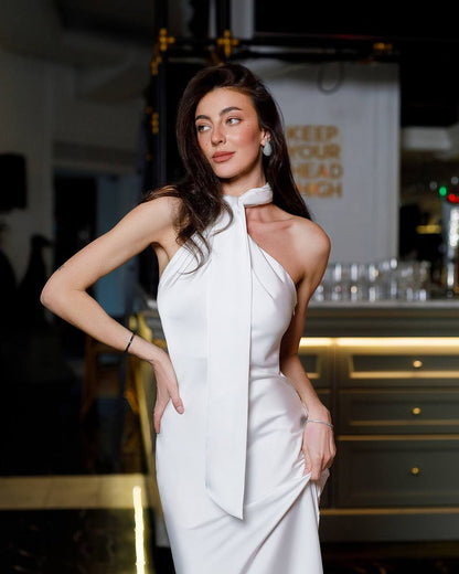 Woman in a white dress posing in an indoor setting with a bar in the background.