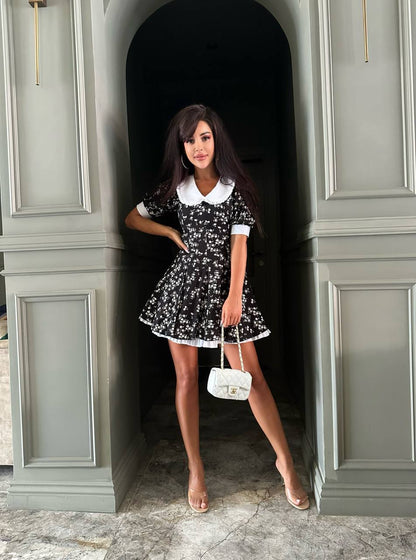 Woman in a black and white dress standing in a doorway with gray walls.