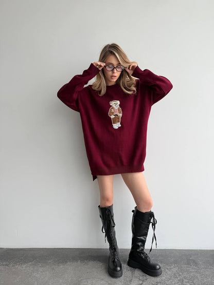 Person wearing a burgundy oversized sweater with a graphic design and black boots against a plain background