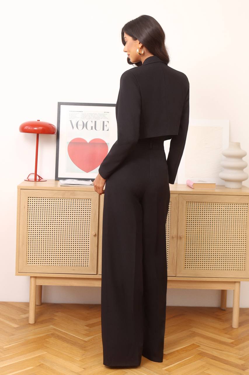 Woman in a black outfit standing in front of a wooden cabinet with a 'Vogue' magazine.