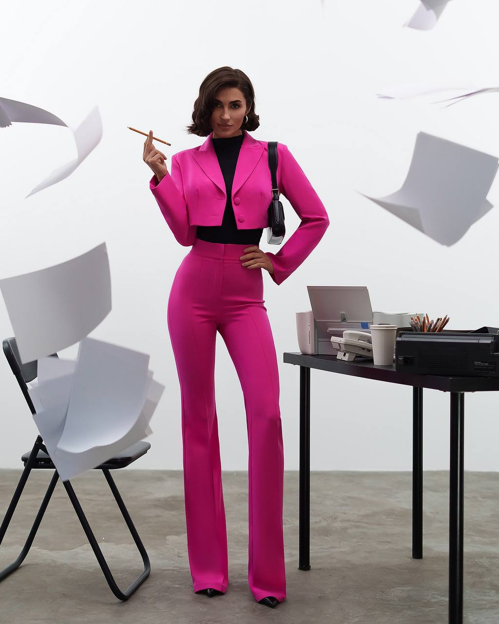 Woman in a bright pink suit standing in an office setting with white chairs and a desk.