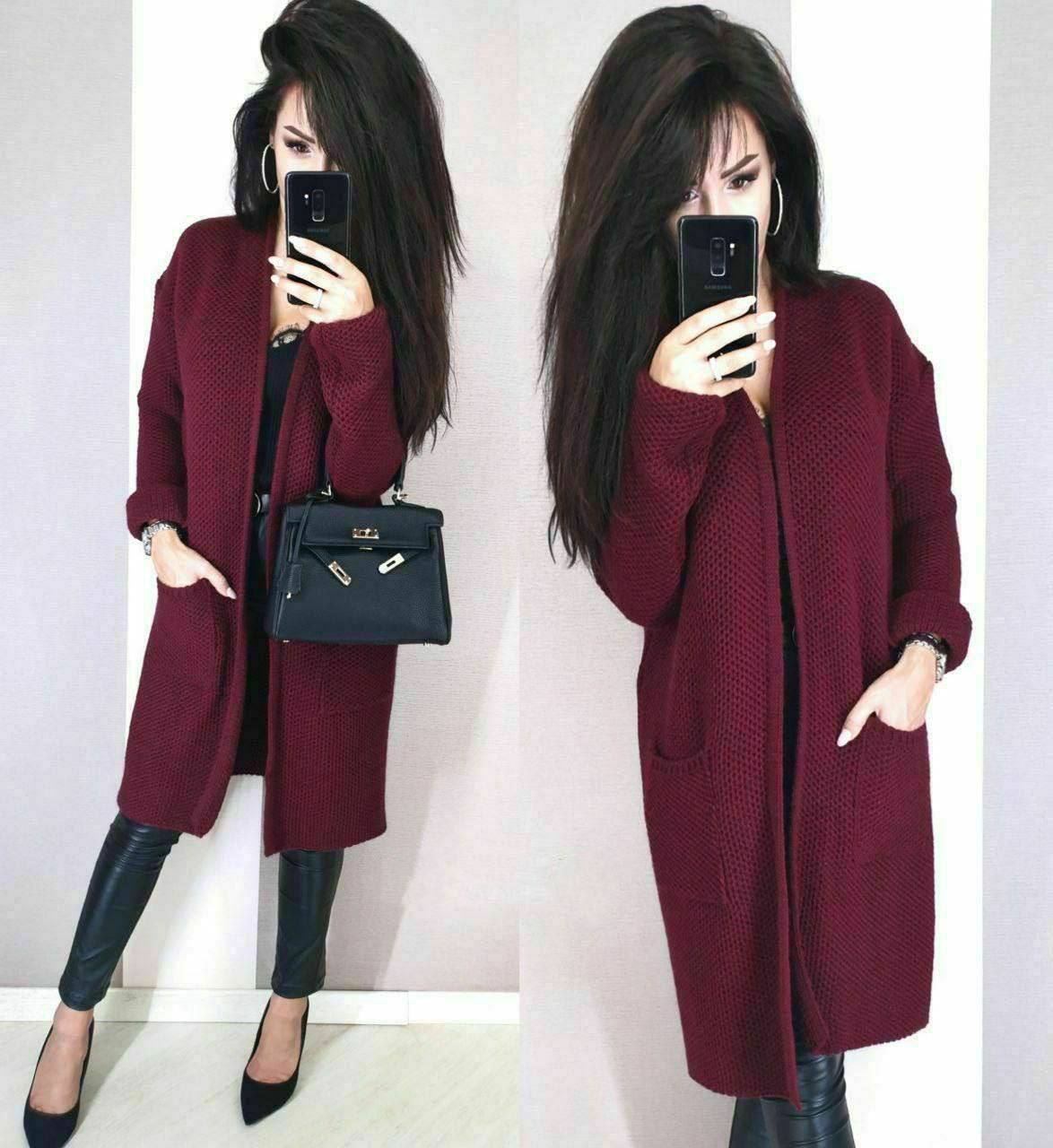 Woman wearing a burgundy coat with a black handbag, standing against a white background.