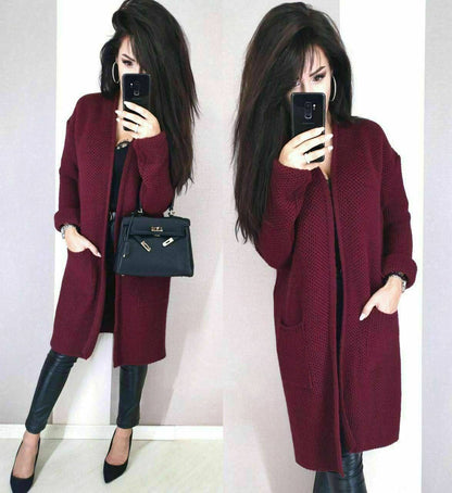 Woman wearing a burgundy coat with a black handbag, standing against a white background.