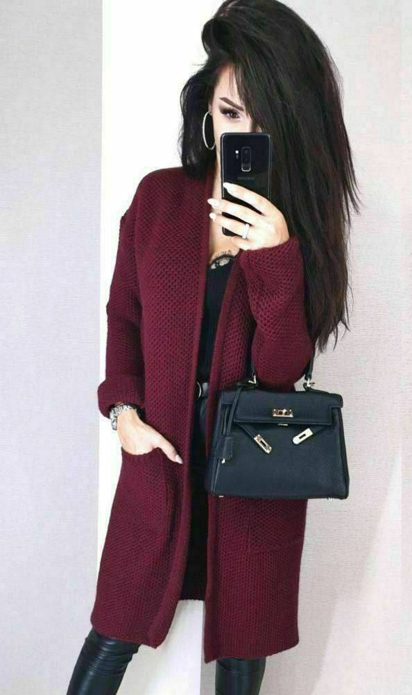 Person wearing a burgundy coat holding a black handbag against a plain background