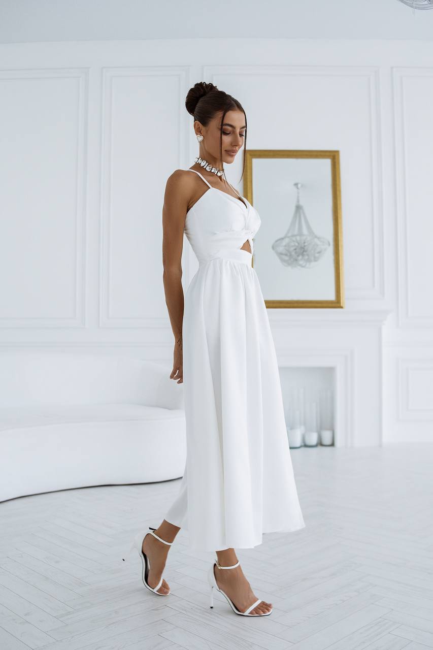 Woman in a white dress standing in a minimalistic room with a chandelier.