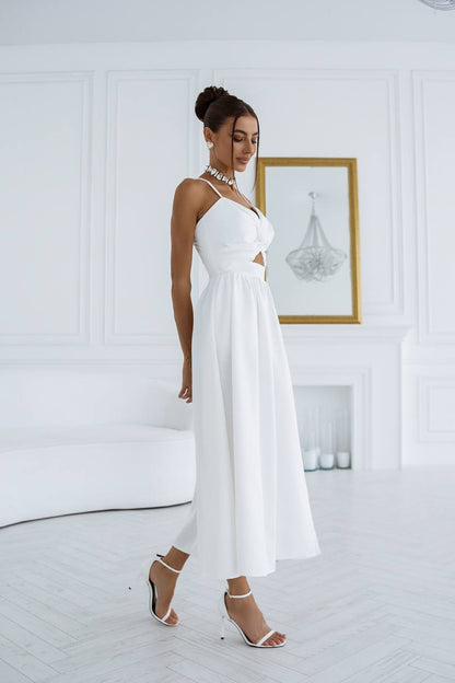 Woman in a white dress standing in a minimalistic room with a chandelier.