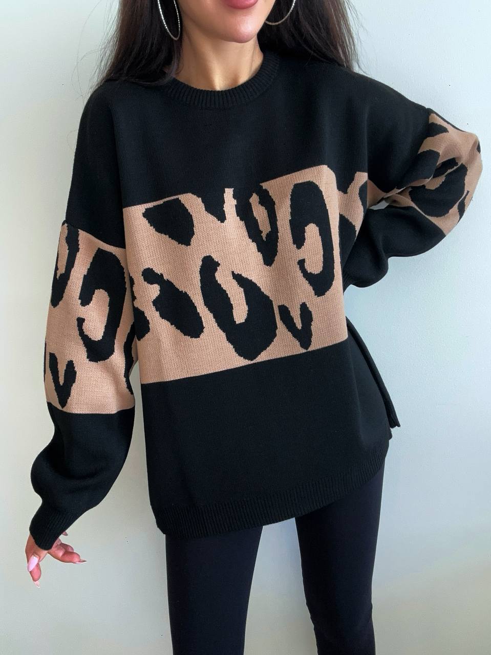Person wearing a black sweater with a beige leopard print design on a plain background