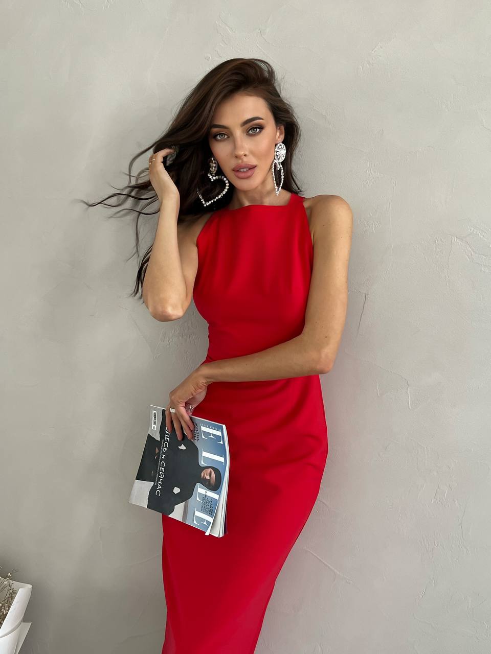 Woman in a red dress holding a magazine against a plain background