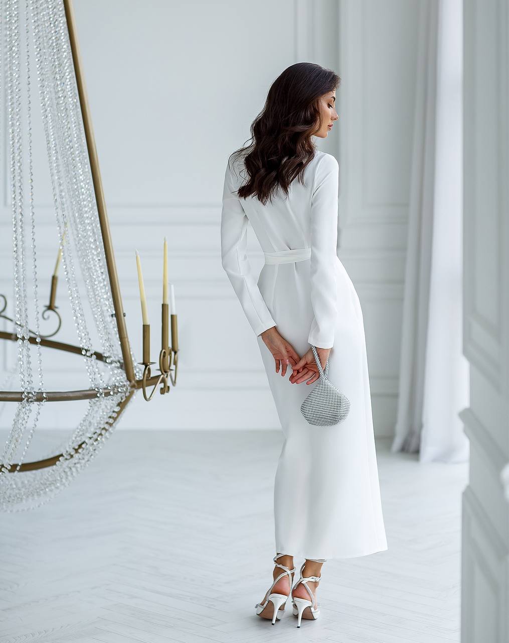 Woman in a white dress standing in a elegant room with a chandelier.