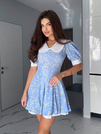 Woman wearing a blue floral dress with a white collar in an indoor setting