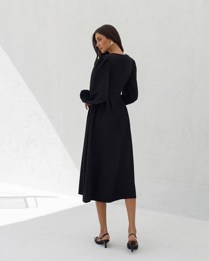 Woman wearing a black dress standing in a minimalistic white room