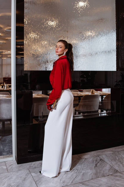 Woman in a red top and white pants standing in a modern interior setting.