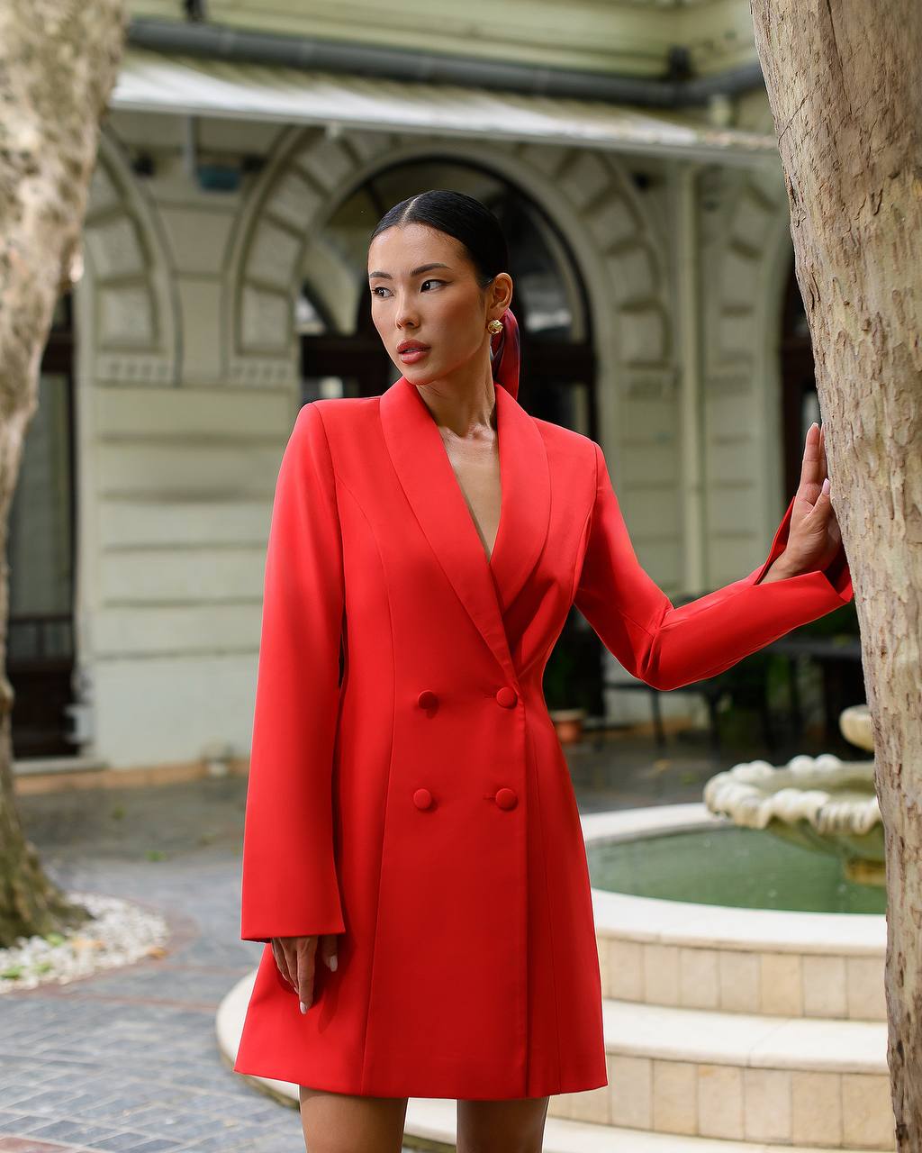 Woman in a red coat standing outdoors near a fountain
