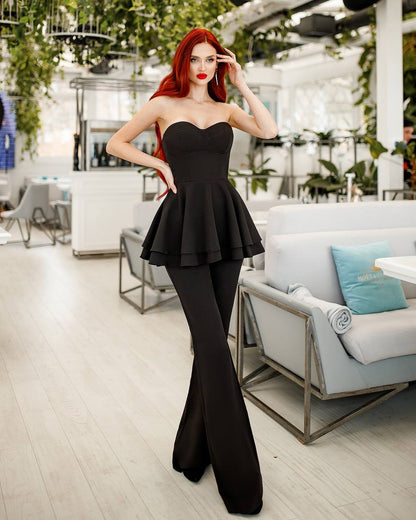 Woman in a black dress standing in an indoor setting with plants and furniture.