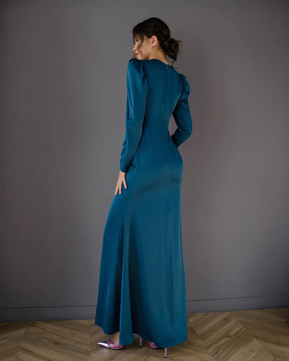 Woman wearing a teal dress standing against a plain wall.