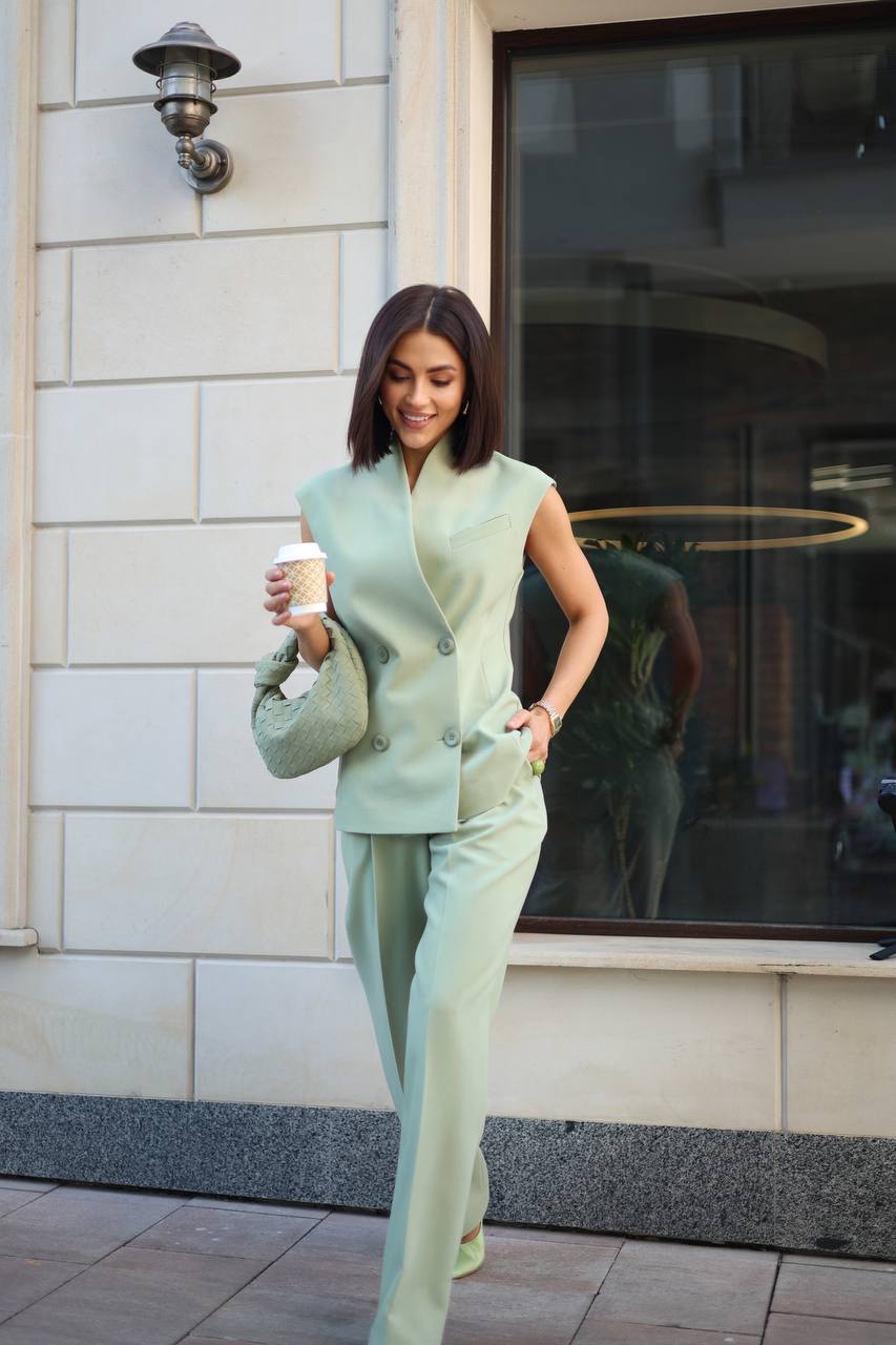 Woman in a light green outfit holding a coffee cup, walking outside a building.