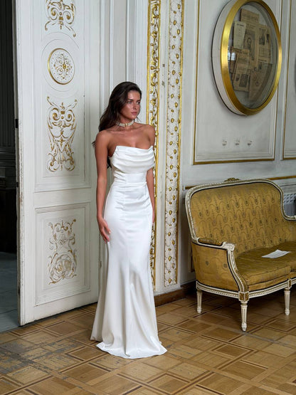 Woman in a white strapless gown standing in an ornate room with decorative walls and furniture.
