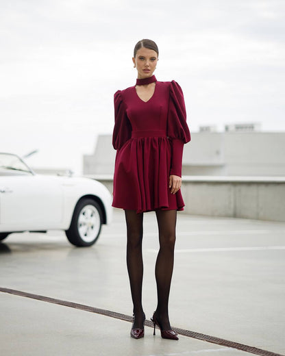 Woman in a burgundy dress standing in a modern indoor setting with a blurred car in the background.
