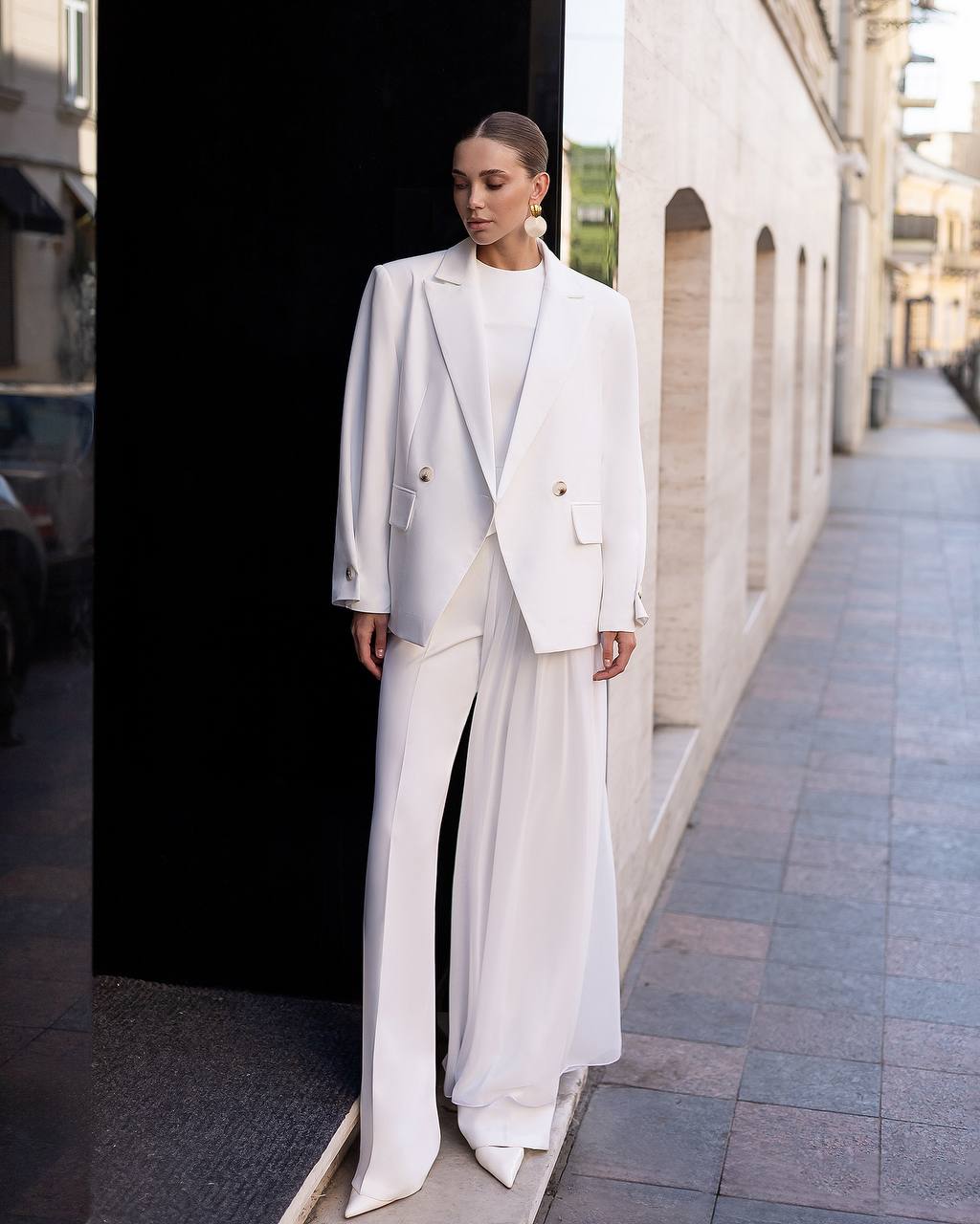 Woman in a white suit standing on a city street.