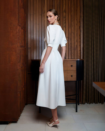 Woman in a white dress standing in a room with wooden paneling.