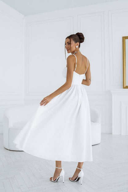 Woman in a white dress standing in a minimalistic room with a white wall and light-colored floor.