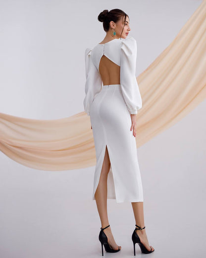 Woman wearing a white dress with cut-out back and high slit, standing against a plain background.