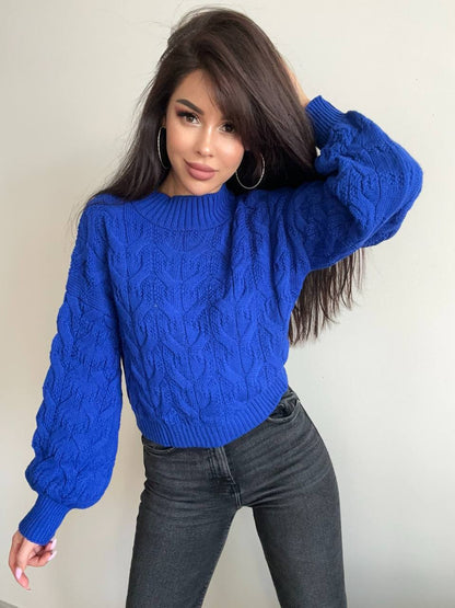 Woman wearing a blue cable knit sweater against a plain background